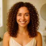 Jeune femme bouclée souriante au teint éclatant, peau lumineuse après une nuit avec la taie en soie SilkDream™.
